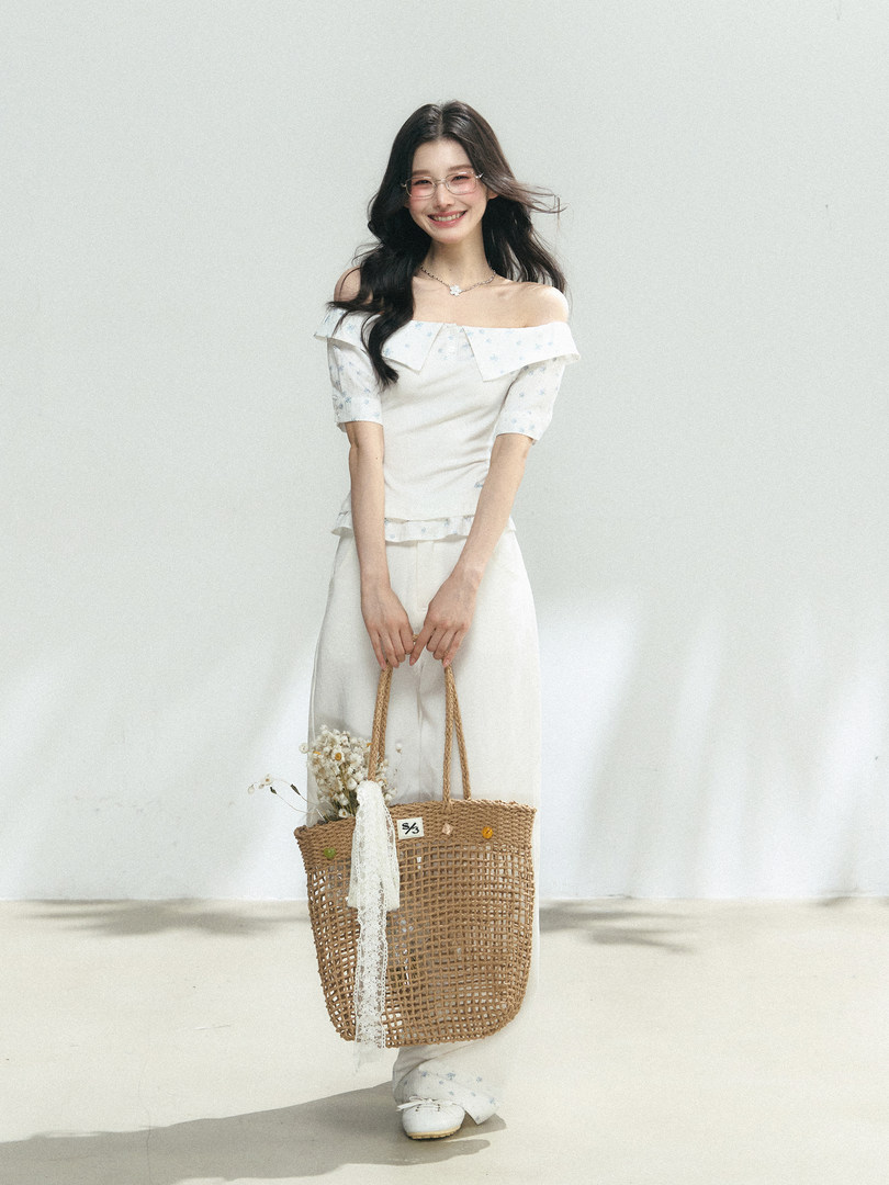 Model wearing a white off-shoulder matching top and pants set with a woven tote bag