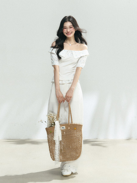Model wearing a white off-shoulder matching top and pants set with a woven tote bag
