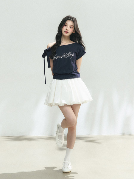 Model wearing a navy off-shoulder top with a white skirt and white shoes