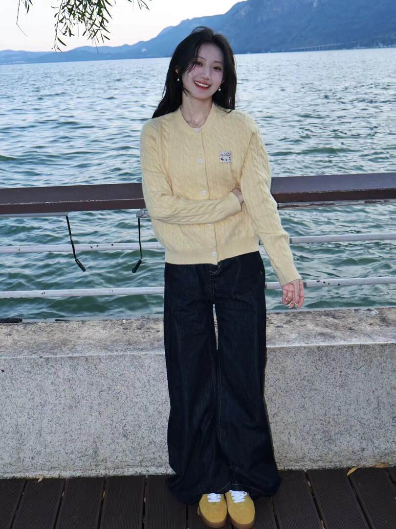 Woman wearing a pale yellow cable-knit cardigan with black wide-leg pants by the waterfront