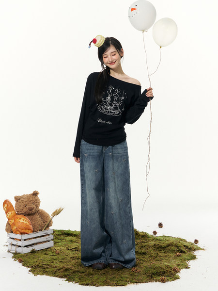 Model wearing a black off-shoulder graphic top and wide-leg blue jeans