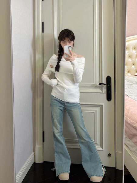 Woman wearing a white off-shoulder top and light blue flared jeans in a mirror selfie