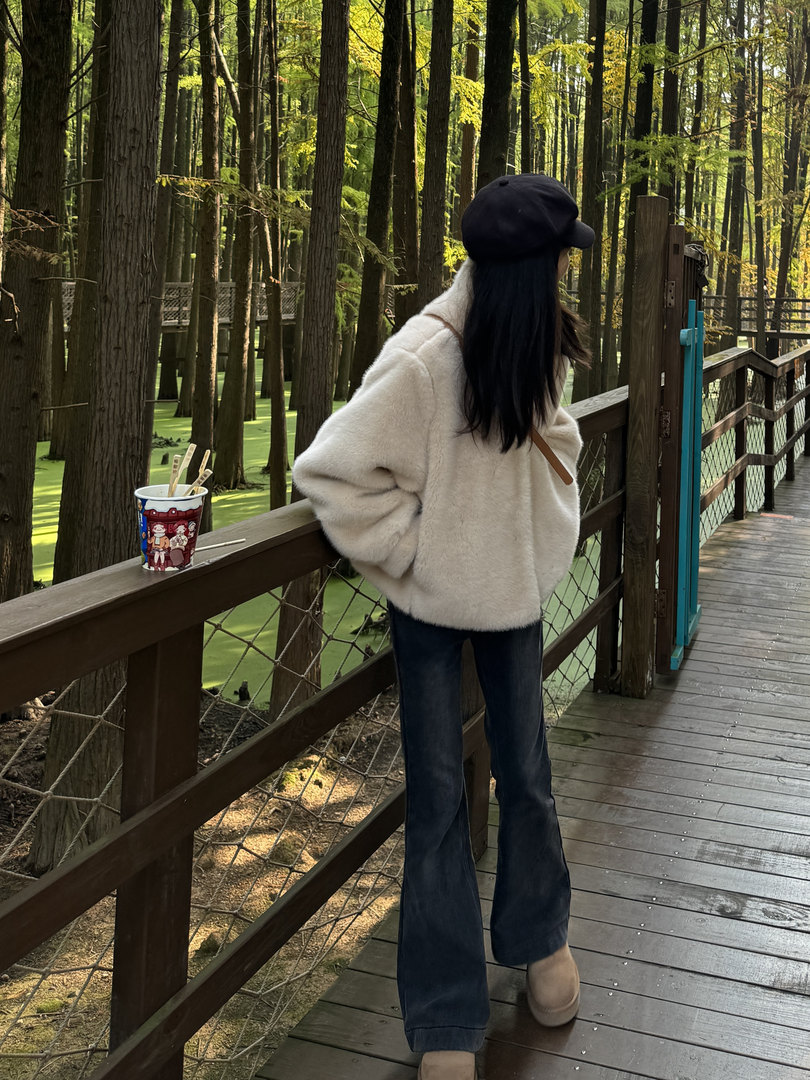 Woman wearing a cream fleece jacket with jeans, black cap, and boots on a forest boardwalk