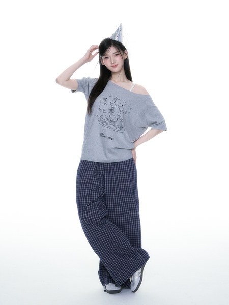 Model wearing a gray graphic off-shoulder top with plaid lounge pants and a party hat