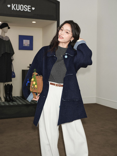 Model wearing a navy wool coat with wide-leg white trousers in a store setting