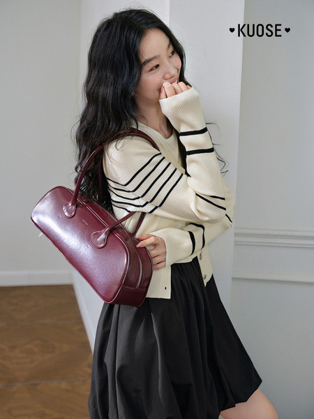 Model wearing a burgundy leather handbag with a cream striped sweater and black skirt