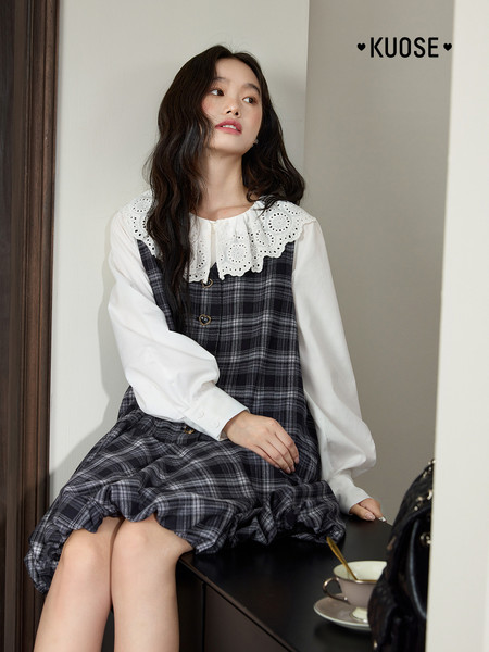Model wearing a plaid pinafore dress with a white blouse