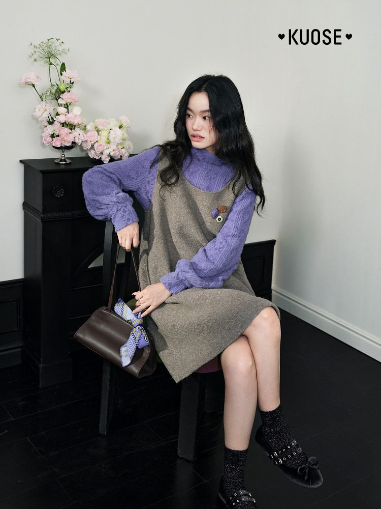 Model wearing a layered purple long-sleeve top with a gray dress and dark handbag