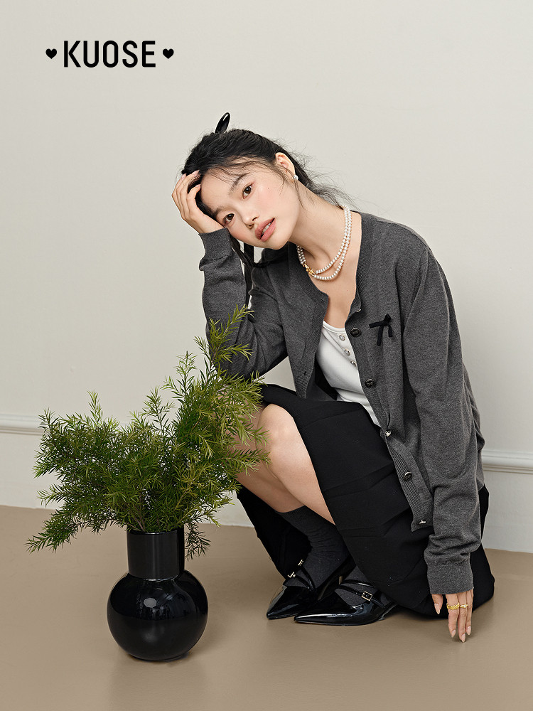 Model wearing a gray cardigan over a white top with a black skirt