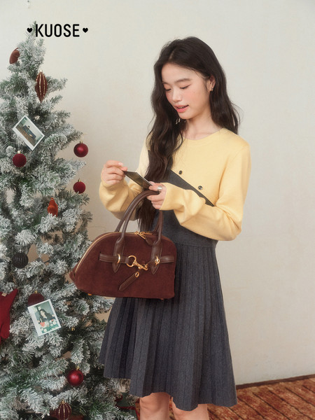 Model in a winter outfit holding a brown leather handbag beside a decorated Christmas tree