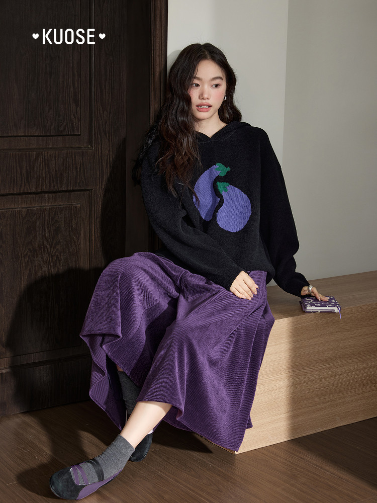 Model wearing a black sweater with purple eggplant graphic and a purple skirt