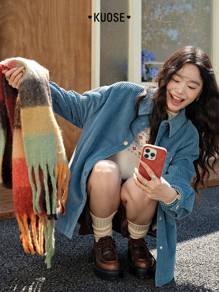 Model wearing a blue corduroy jacket and holding a striped scarf