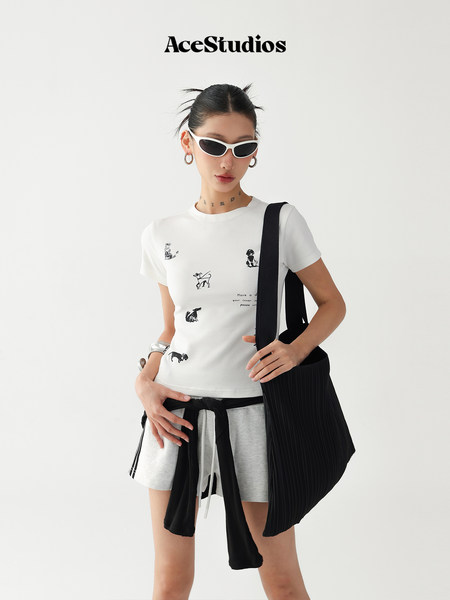 Model wearing a white graphic T-shirt with gray shorts, sunglasses, and a black tote bag