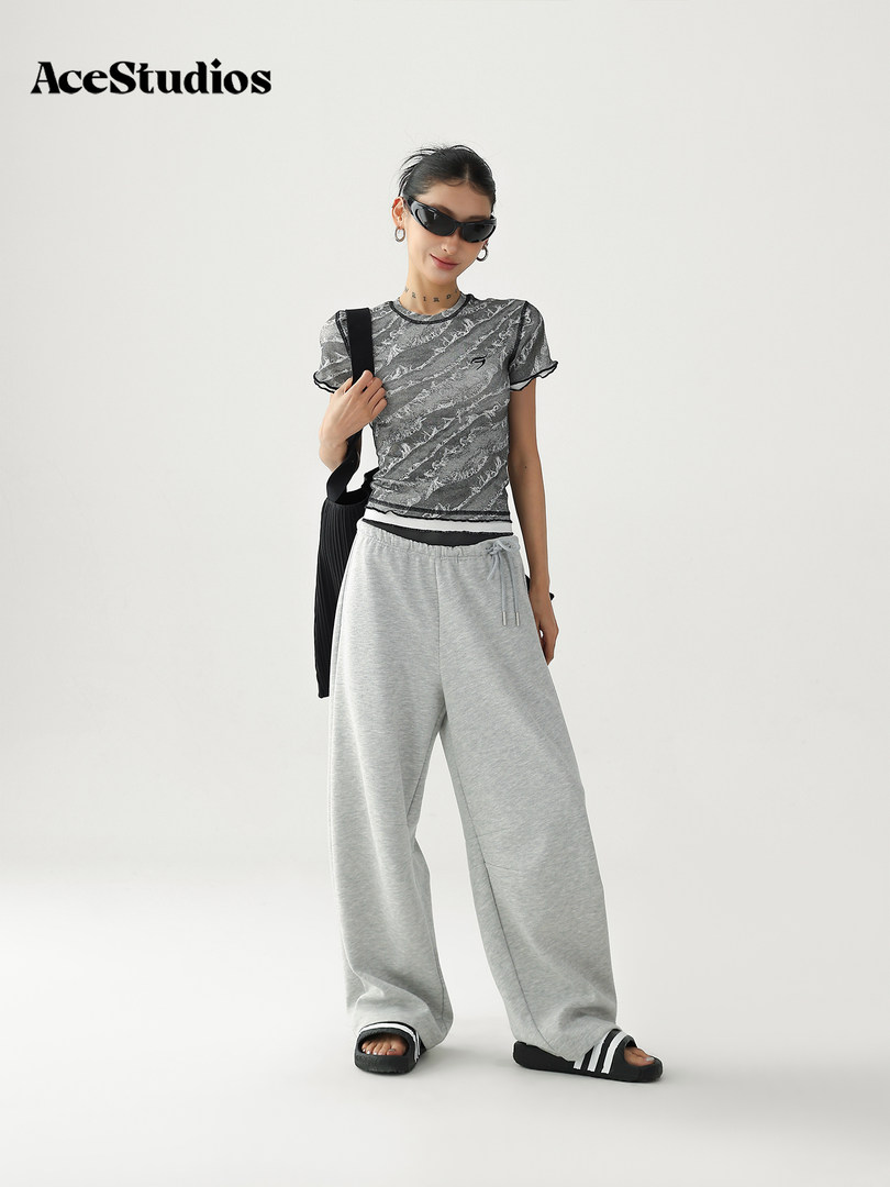 Model wearing a gray graphic tee with oversized light gray sweatpants and black slides