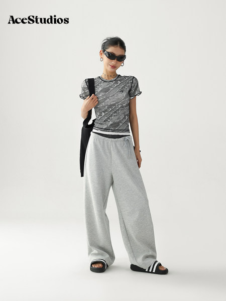 Model wearing a gray graphic tee with oversized light gray sweatpants and black slides