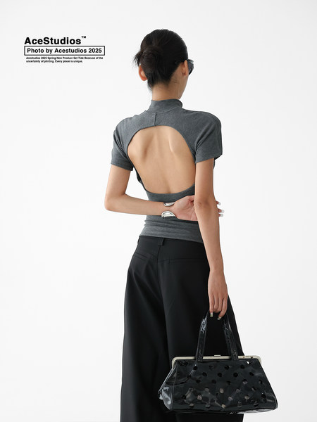 Model wearing a gray open-back top and black wide-leg pants holding a black handbag.