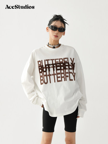 Model wearing a white graphic long-sleeve top with "BUTTERFLY" print and black biker shorts