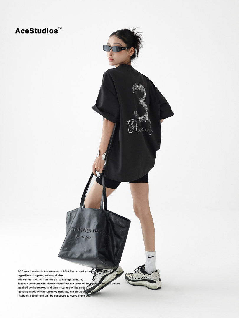 Model wearing an oversized black graphic T-shirt and carrying a black tote bag