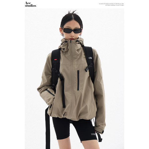 Model wearing a beige hooded zip-up jacket with black backpack and cycling shorts