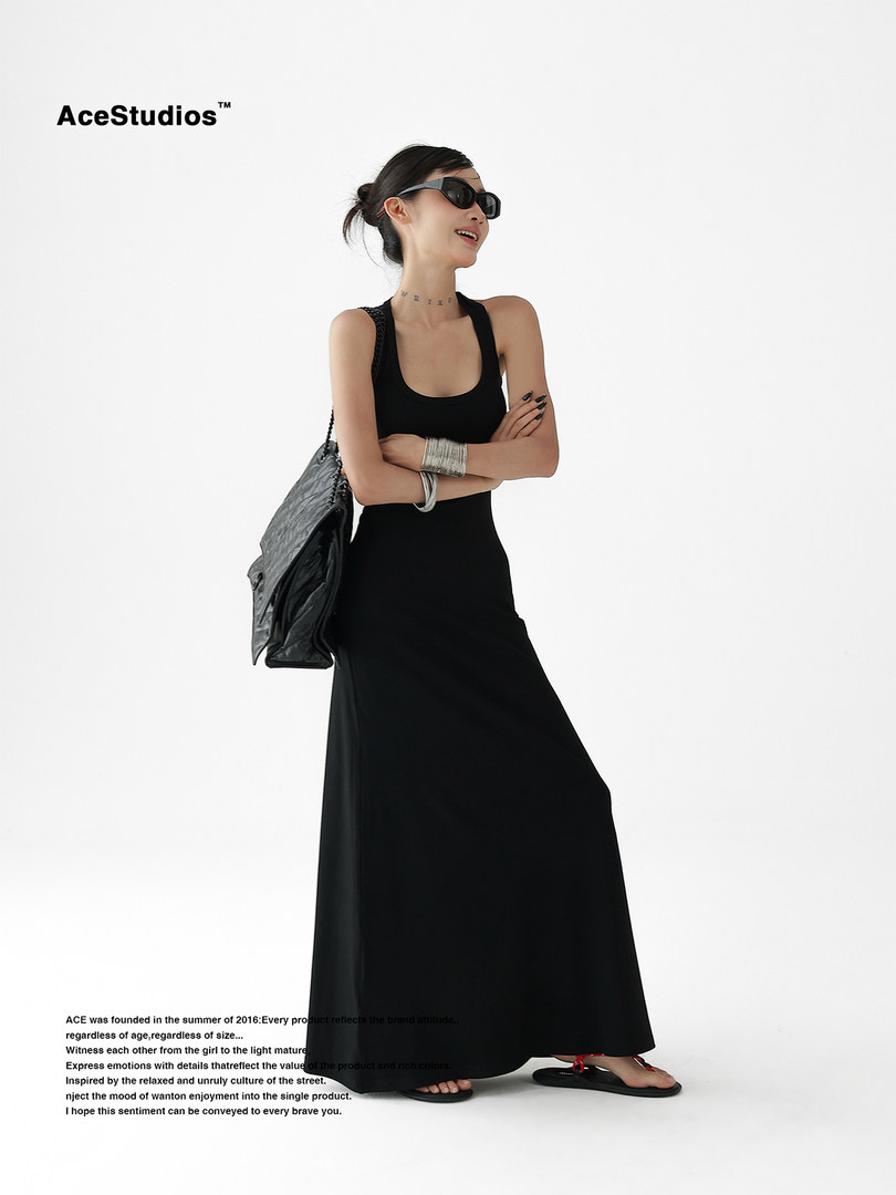Model wearing a black sleeveless maxi dress with a shoulder bag on a white background