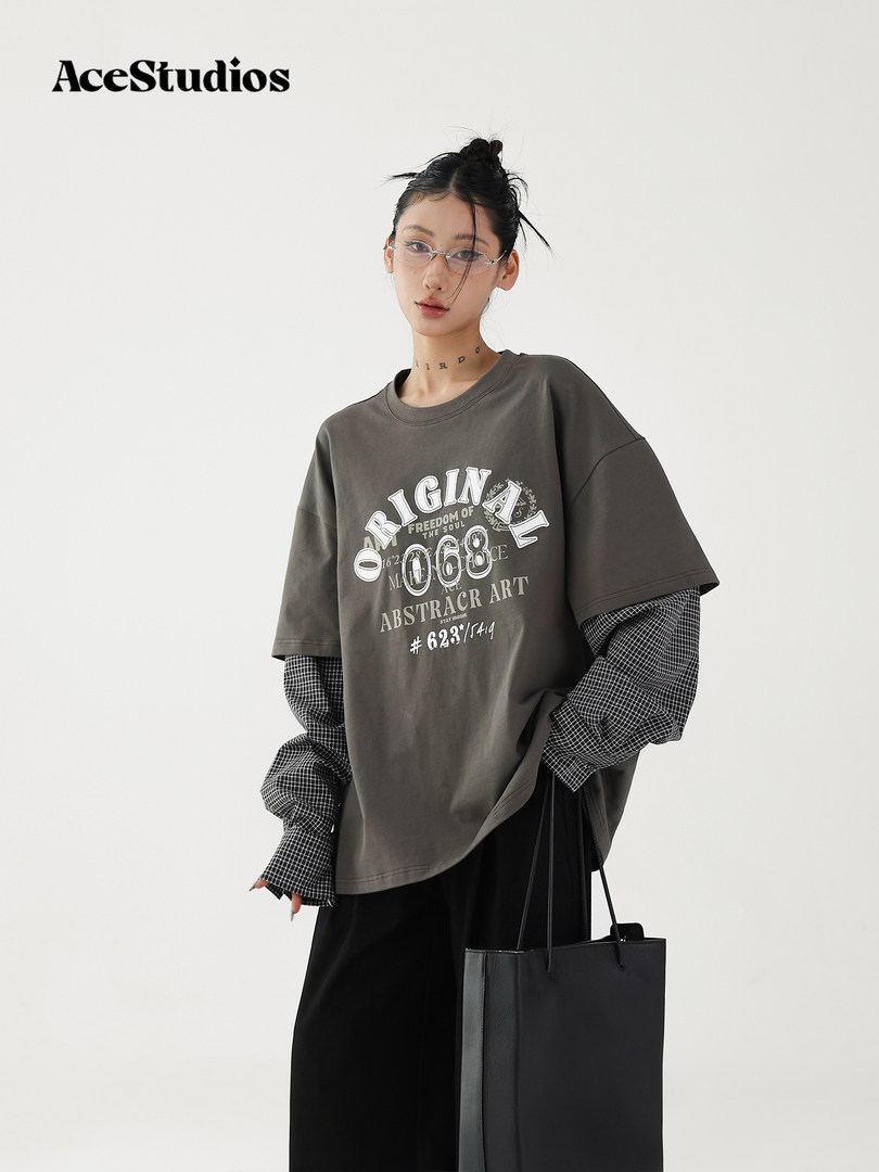Model wearing an oversized graphic T-shirt layered over a checkered long-sleeve top with a black tote bag