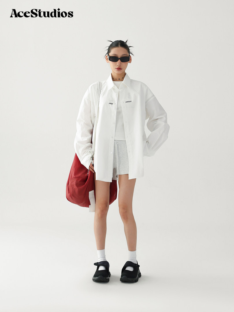 Model wearing an oversized white shirt with shorts and black shoes on a plain background