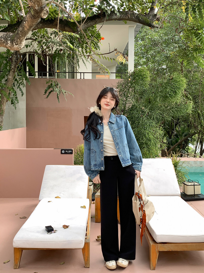 Woman wearing a light blue denim jacket with black wide-leg pants outdoors