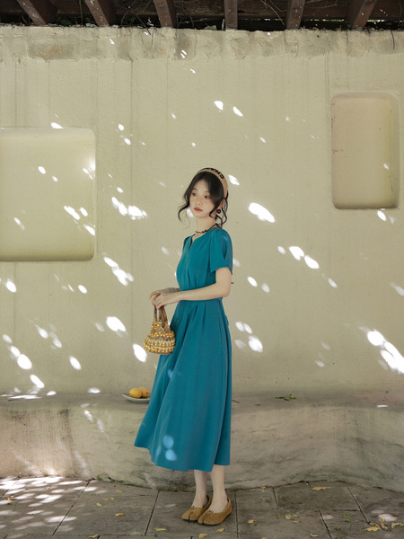 Woman wearing a teal midi dress and holding a small handbag outdoors