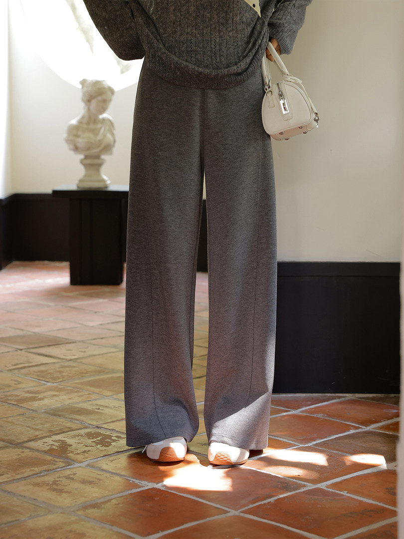 Model wearing wide-leg gray pants with a knit sweater and white handbag