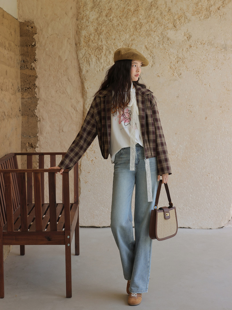 Woman modeling a plaid jacket, graphic top, jeans, beret, and handbag