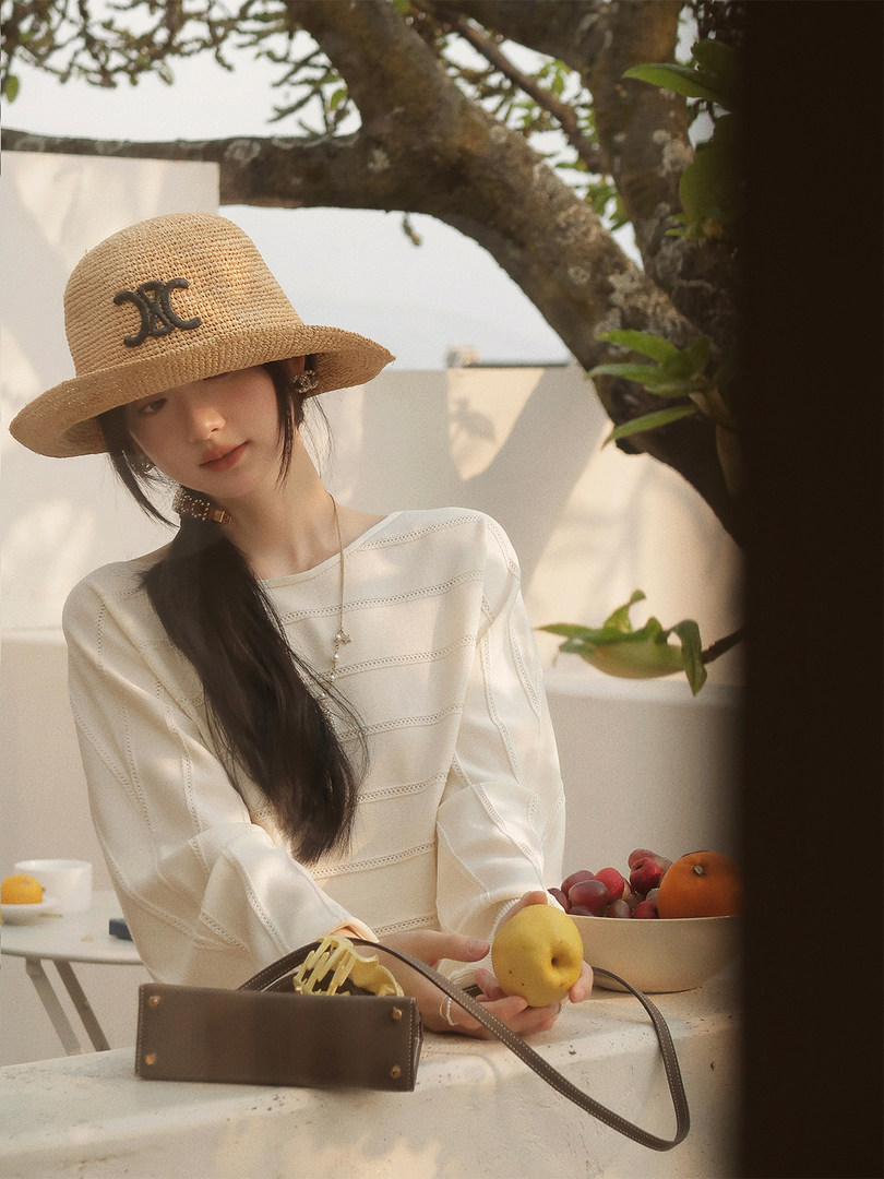Woman wearing a straw hat, white blouse, and small brown handbag outdoors