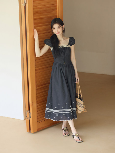 Model wearing a black embroidered midi dress with puff sleeves and a woven tote bag