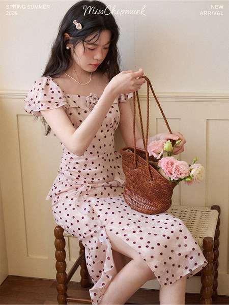 Woman wearing a pink polka dot dress while holding a woven basket of flowers