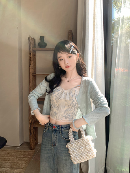 Woman wearing a floral lace cami top with a light knit cardigan and jeans, holding a pearl handbag