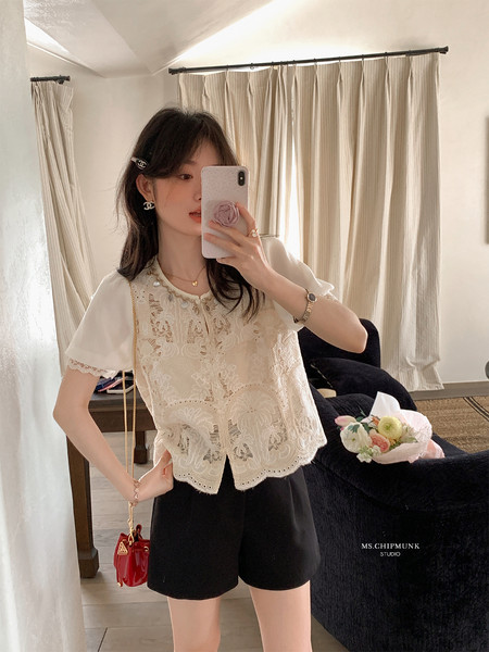 Woman wearing a cream lace short-sleeve top and black shorts in a mirror selfie
