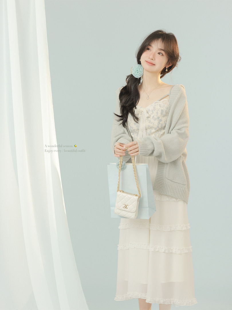 Woman modeling a light pastel cardigan over a lace dress with a small chain handbag
