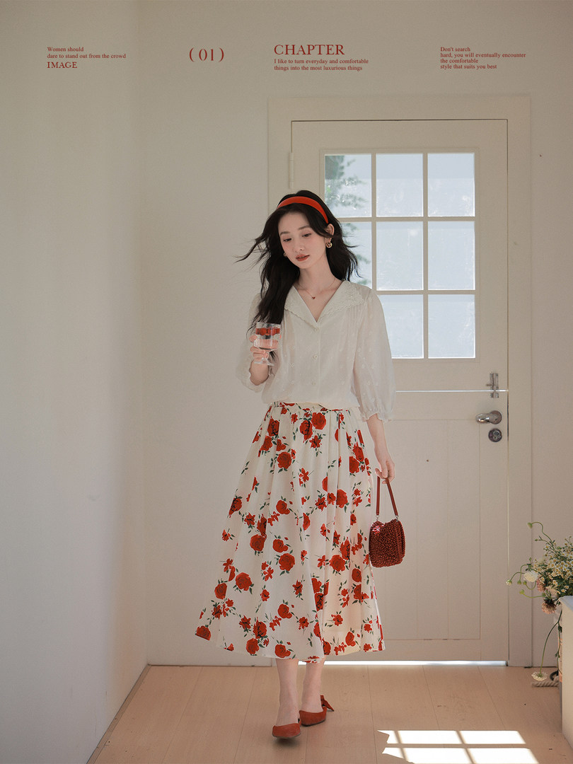 Woman wearing a white blouse with a red floral midi skirt and small handbag
