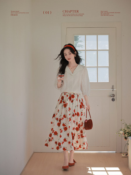 Woman wearing a white blouse with a red floral midi skirt and small handbag