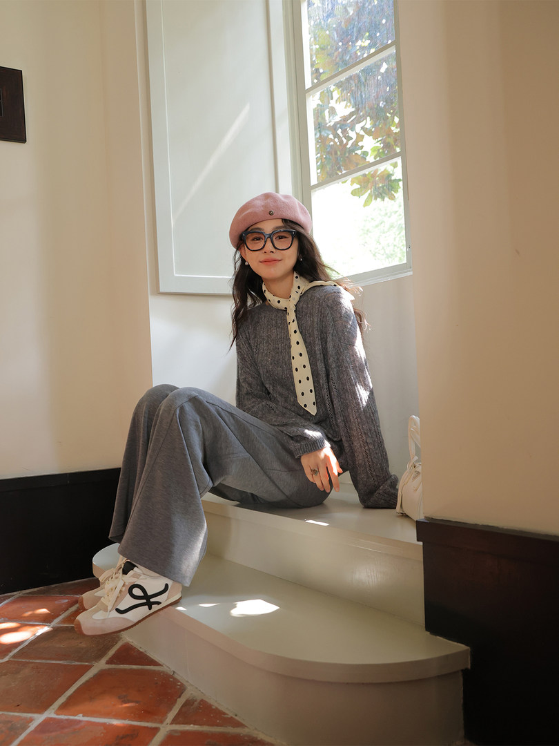 Woman wearing a gray outfit with a pink beret and white sneakers seated by a window
