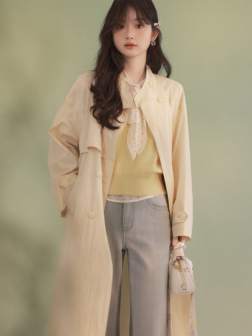 Model wearing a beige trench coat layered over a pale top with jeans and a small handbag