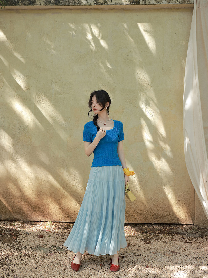 Woman wearing a bright blue knit top with a light blue pleated maxi skirt