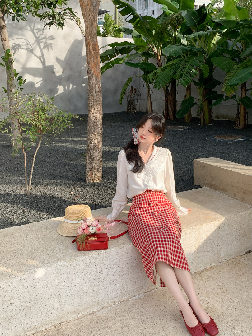 Woman wearing a white blouse and red gingham skirt with red flats outdoors