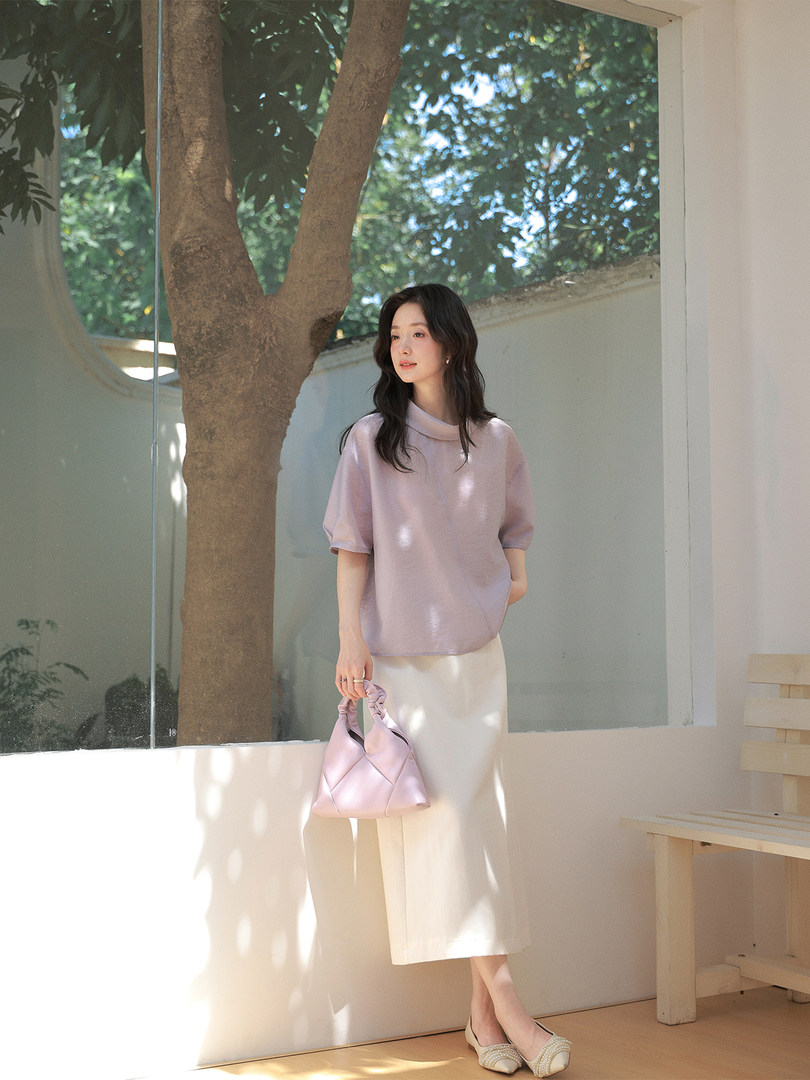 Model wearing a light lavender blouse with a cream midi skirt and matching handbag