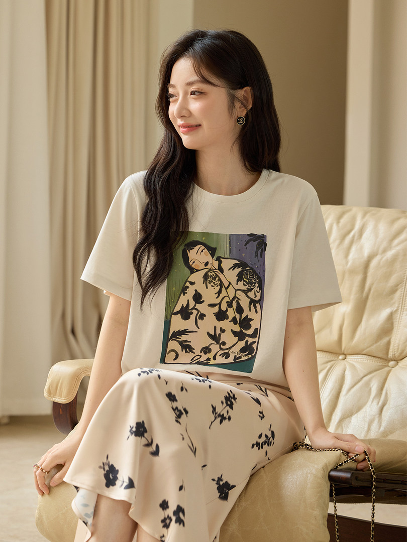 Woman wearing a cream graphic tee and floral skirt lounge set on a sofa