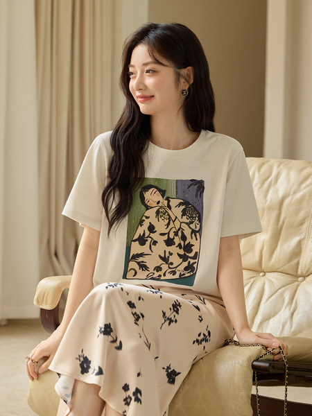 Woman wearing a cream graphic tee and floral skirt lounge set on a sofa