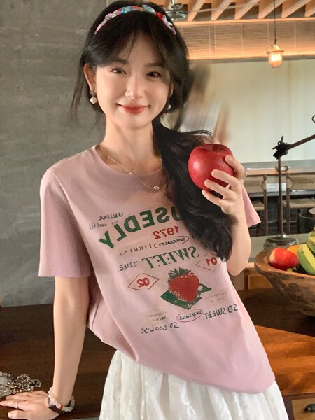 Woman wearing a pink graphic T-shirt and holding a red apple indoors