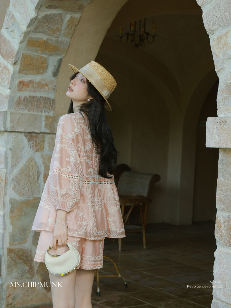 Woman wearing a pink embroidered dress and straw hat holding a white handbag