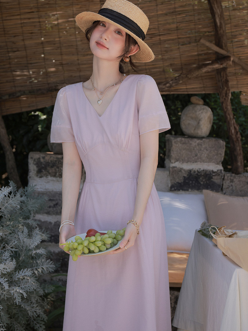 Woman wearing a light pink V-neck dress and straw hat outdoors