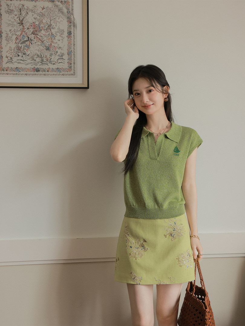 Model wearing a green knit sleeveless top with a matching floral mini skirt and woven handbag