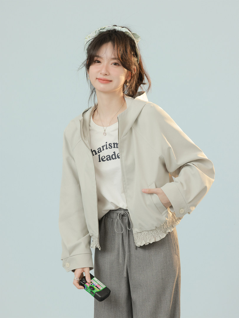 Woman modeling a light beige jacket with white graphic tee and gray pants